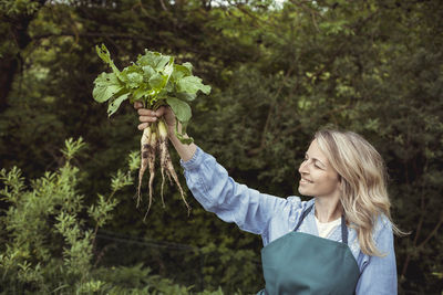 Midsection of woman holding plants against trees