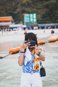 Woman photographing through smart phone while standing at beach