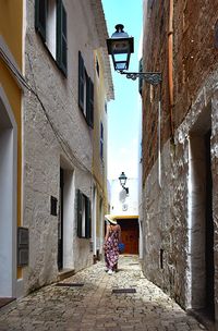 Rear view of woman walking on narrow alley amidst buildings