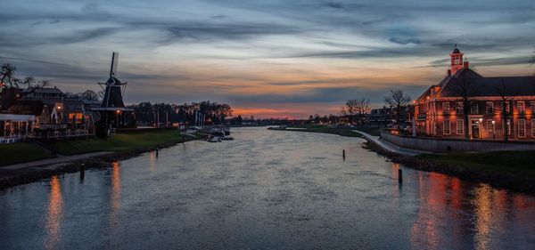 River by illuminated buildings against sky at sunset