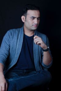 Thoughtful man looking down while sitting against black background