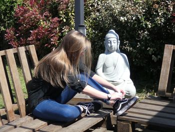 Woman sitting on bench against plants