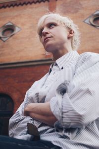 Low angle view of young woman looking away while sitting against wall
