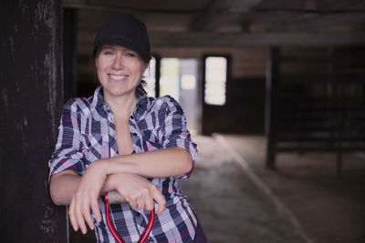 Portrait of happy female farmer with pitchfork standing at entrance of barn