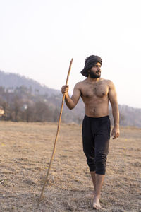 Young indian farmer with a stick walking in a wasteland. crops not growing due to shortage of rain