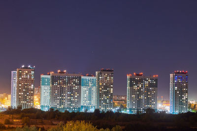 Illuminated buildings in city against clear sky at night