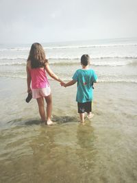 Rear view of siblings standing on beach against sky