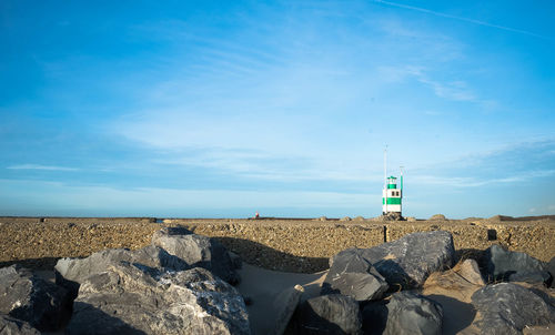 Lighthouse by rocks against blue sky