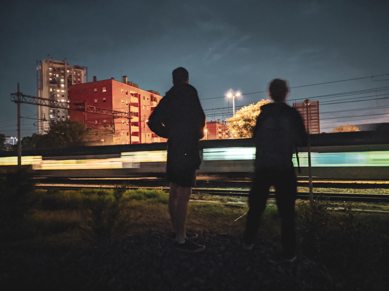 REAR VIEW OF MAN STANDING BY RAILING IN CITY AGAINST SKY