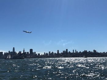 Airplane flying over buildings in city against sky