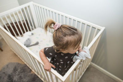 High angle of blonde toddler girl in crib bed.