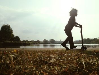 Silhouette girl riding push scooter against sky