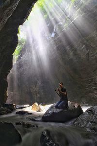 Close-up of man praying while sitting on rock at river against sky