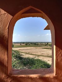 Nature theories- scenic view of field against sky seen through arched window