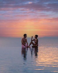 Rear view of woman swimming in sea against sky during sunset