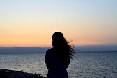 Rear view of woman standing by sea against sky during sunset