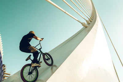 Low angle view of man riding bicycle on built structure against sky
