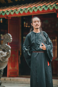 Portrait of young woman standing against building