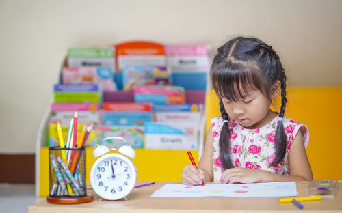 Cute girl drawing on paper while sitting on table at home