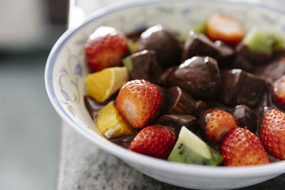 Bowl with pieces of fresh fruits and liquid chocolate in home kitchen