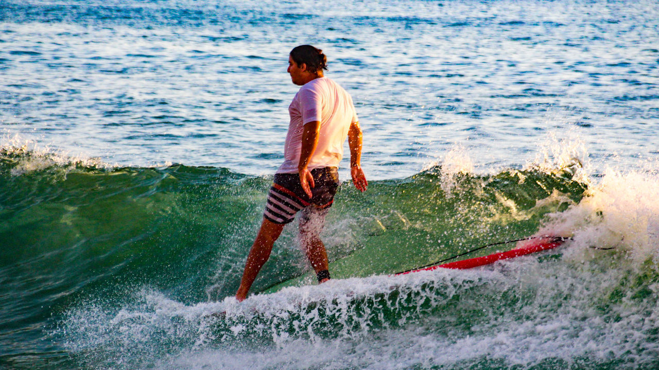 FULL LENGTH OF SHIRTLESS MAN SPLASHING WATER IN SEA