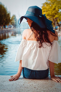 Rear view of woman sitting on retaining wall against canal