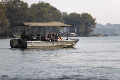 People sitting in boat in river against trees