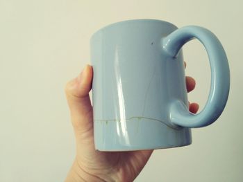 Close-up of hand holding coffee cup over white background