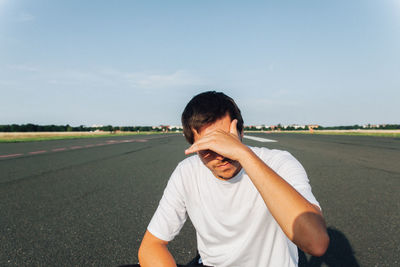 Man shielding eyes on road against sky