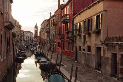 Boats moored in canal amidst buildings during sunrise