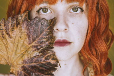 Portrait of woman with dry leaf standing against wall