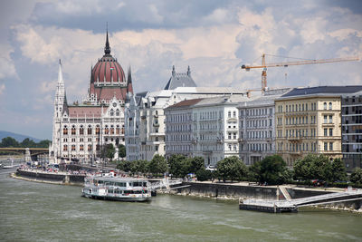 Hungarian parliament building by danube river against sky in city