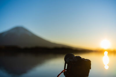 Rear view of man standing by lake against clear sky during sunset