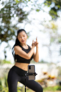 Young woman using phone while standing on tree