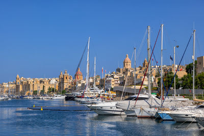 Sailboats moored in harbor by buildings against clear blue sky