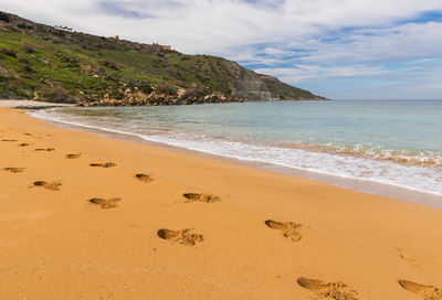Footprints in sand at ramla bay in gozo island, malta. scenic view of beach against sky
