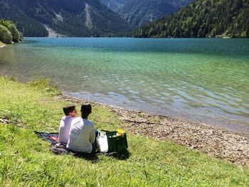 Rear view of man sitting on grass by lake