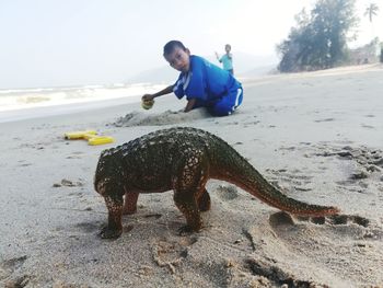 Boy with artificial dinosaur at sea shore