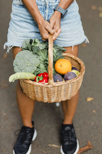 Woman holding vegetable basket while standing on road at park