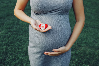 Midsection of pregnant woman holding canadian flag in heart shape