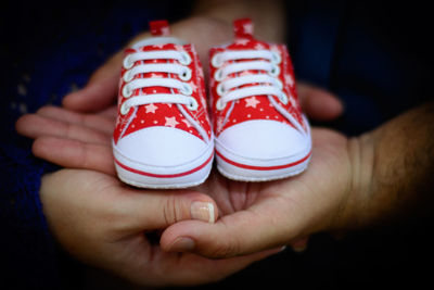 Cropped hands of couple holding small shoes in darkroom