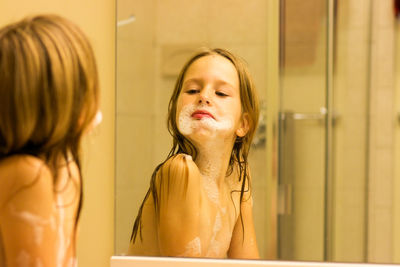 Topless girl with soap sud looking in mirror at bathroom