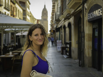 Portrait of smiling young woman on street amidst buildings in city