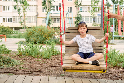 Little boy riding a swing in a green park. happy childhood. a boy rides on a wide swing, close-up. 