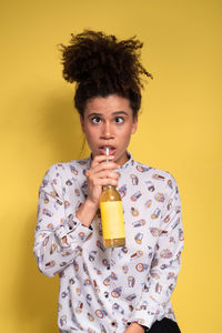 Portrait of young woman holding drink against yellow background