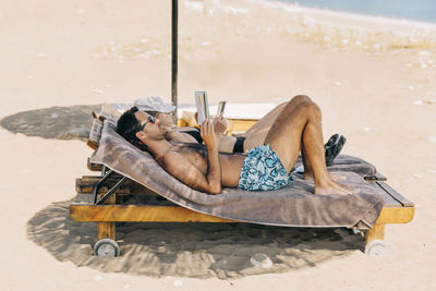 Full length of shirtless man relaxing at beach