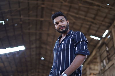 Low angle view of young man looking away while standing indoors