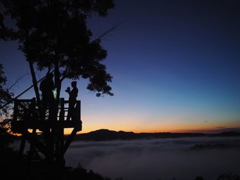 Silhouette trees by plants against sky during sunset