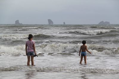 Rear view of men at beach against sky