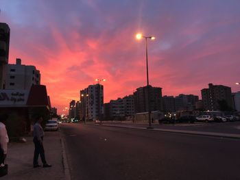 People walking on road against buildings at sunset